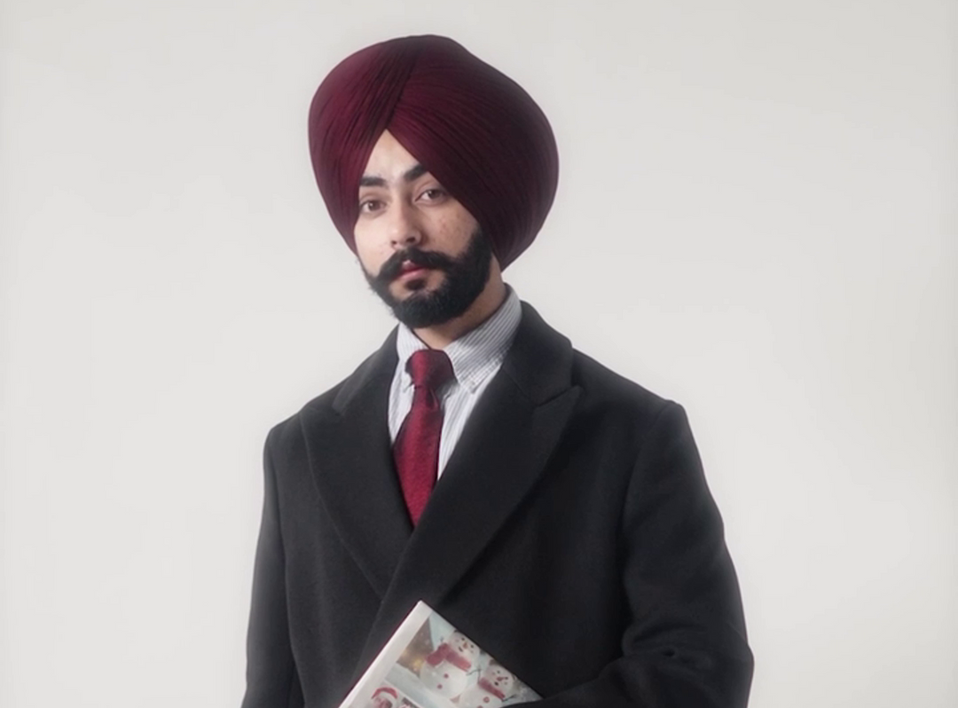 a sikh man standing wearing a long overcoat blazer and maroon full voile turban